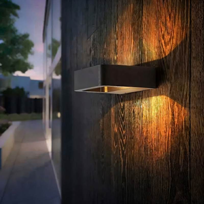 Clérachic black wall light on dark wood cladding at dusk, its warm light fanning up and down beside a glazed walkway.