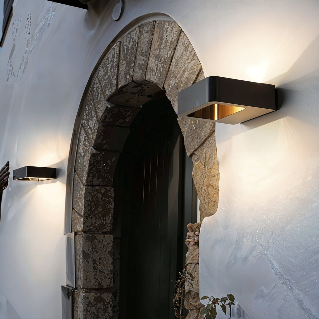 Two Clérachic black wall lights lit beside a stone arched doorway on a pale rendered wall at dusk.