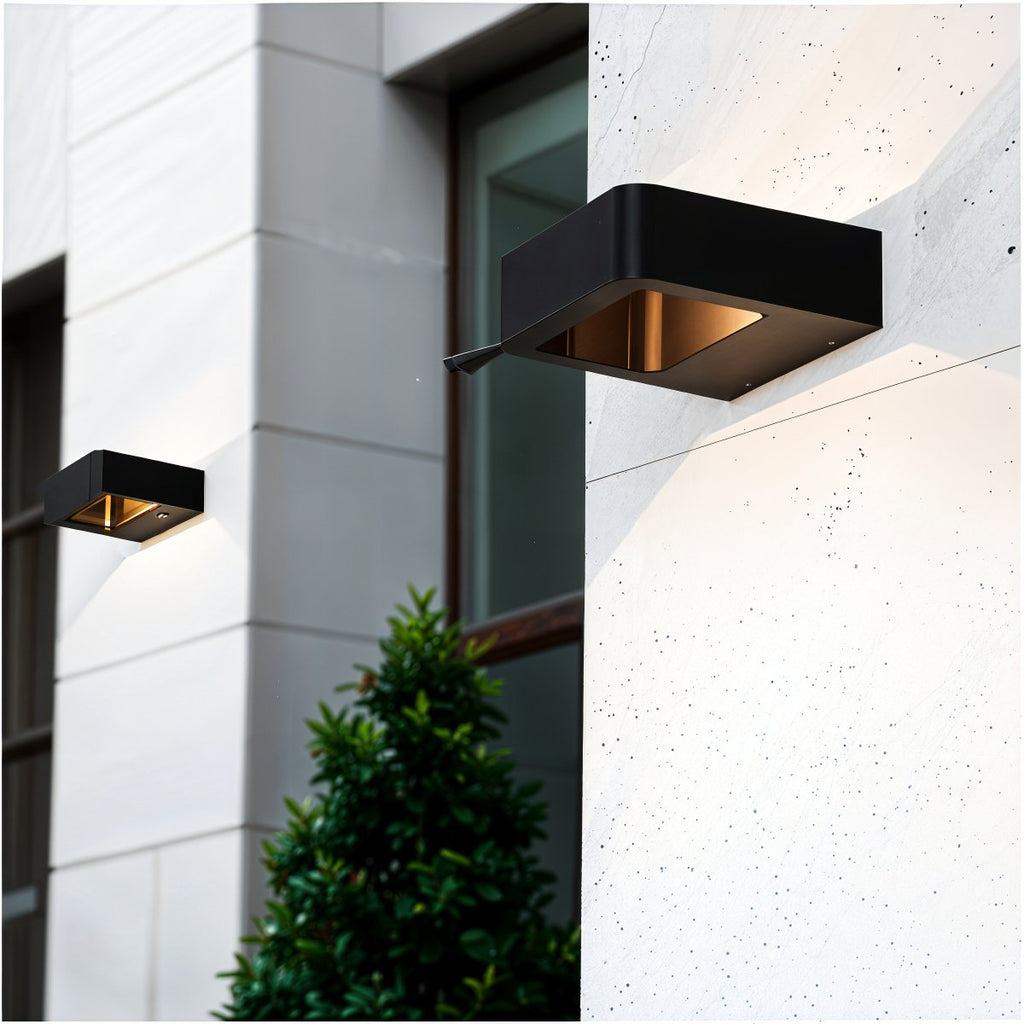 Two Clérachic black wall lights with brass-toned interiors on a pale stone and white facade, a shrub below the windows.