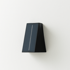 Clérachic solar wall light in black with a tilted solar panel on one face, mounted on a plain white wall, switched off.