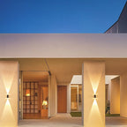 Clérachic solar wall lights mounted on pale pillars of a covered entrance, each casting a warm cone of light up and down at dusk.