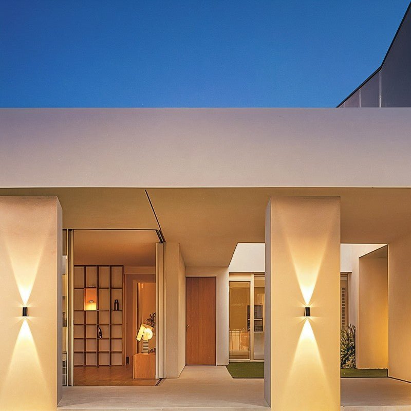 Clérachic solar wall lights mounted on pale pillars of a covered entrance, each casting a warm cone of light up and down at dusk.