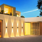 Row of four Clérachic solar wall lights on a pale rendered wall, each throwing a warm up-and-down beam in the evening.