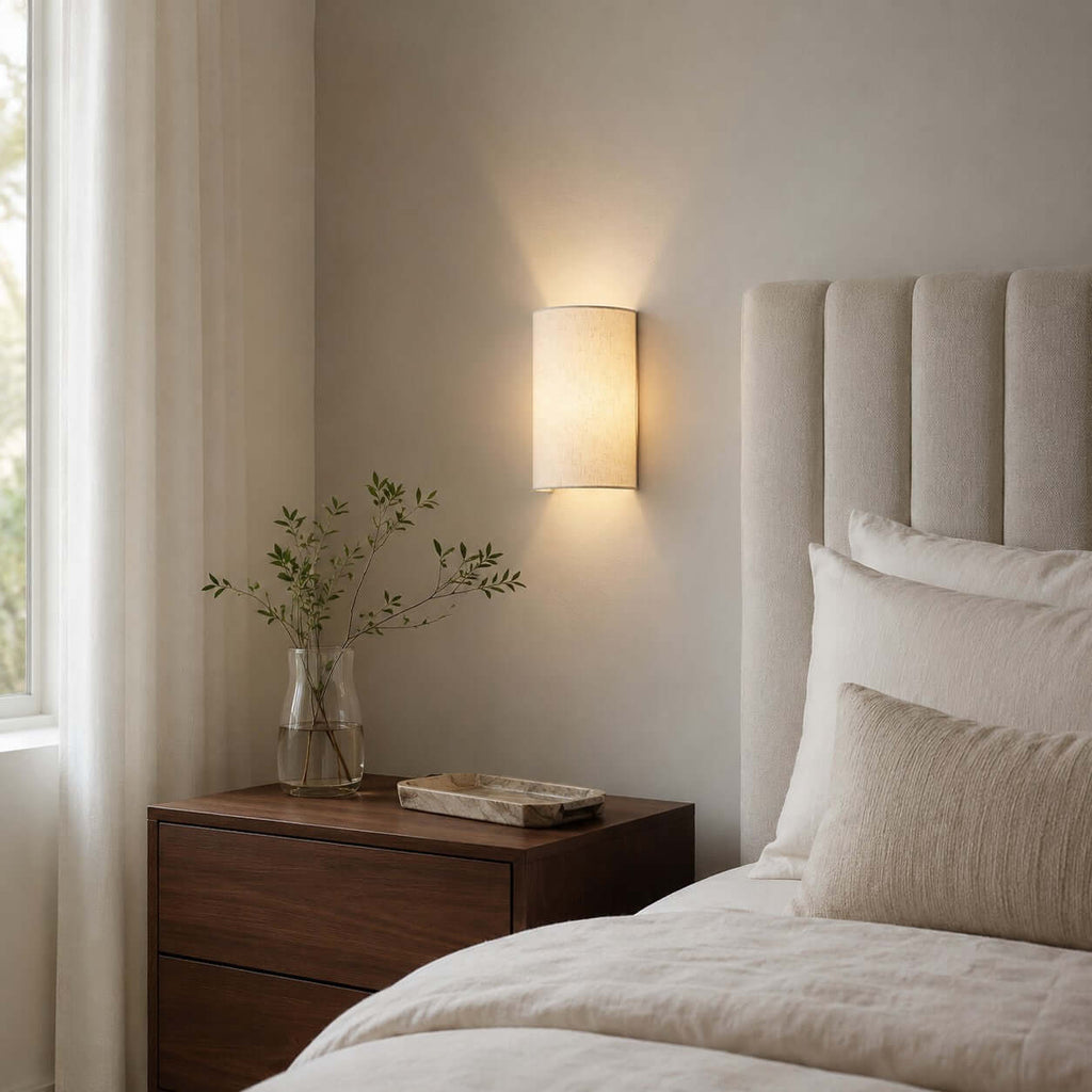 Clérachic half-round wall light glowing above a walnut bedside table, beside a ribbed headboard and a sheer curtain.