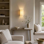 Clérachic wall light above a small console in a reading nook, with built-in shelves and a window seat with a cushion.