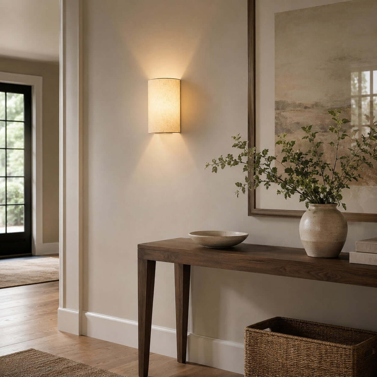 Clérachic fabric wall light above a dark wood console with a bowl and a large vase of green stems, beside a glazed door.