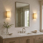 Pair of Clérachic wall lights either side of a tall framed mirror above a washbasin, with a green sprig in a glass vase.
