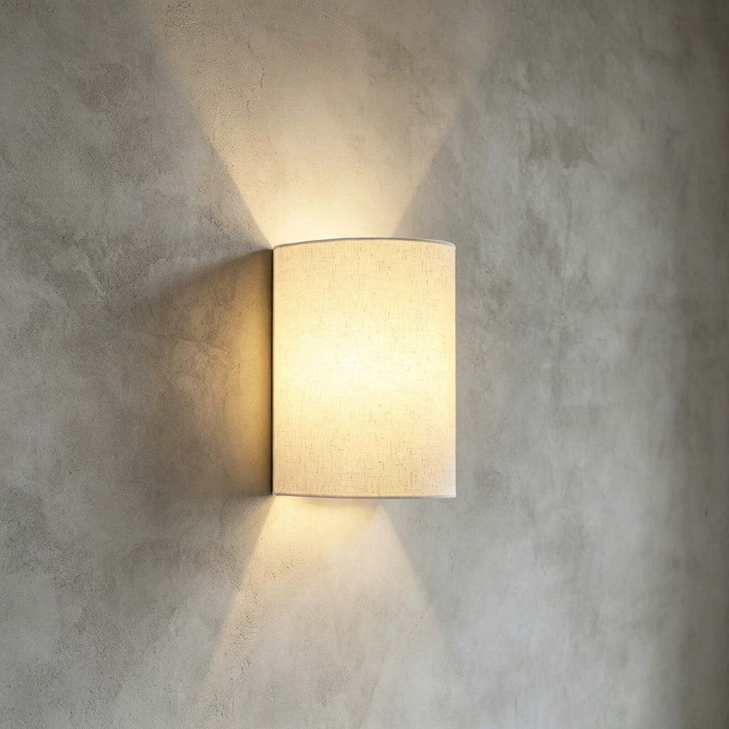 Close view of the linen-textured half-round shade on this Clérachic wall light, casting light up and down a grey plaster wall.