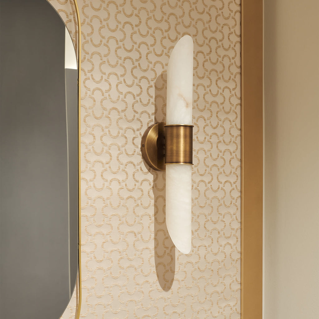 The Clérachic Up-Down Wall Sconce mounted on patterned cream wallpaper beside a gold-framed mirror in a powder room.