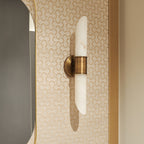 The Clérachic Up-Down Wall Sconce mounted on patterned cream wallpaper beside a gold-framed mirror in a powder room.