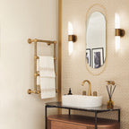 A pair of Clérachic Up-Down Wall Sconces lit either side of an oval mirror above a marble-top bathroom vanity.