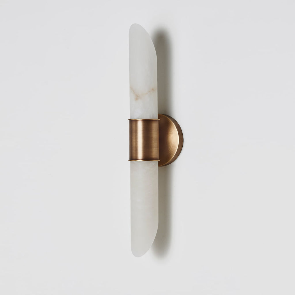Angled view of the Clérachic Up-Down Wall Sconce on a pale grey wall, showing the aged brass collar and round backplate.