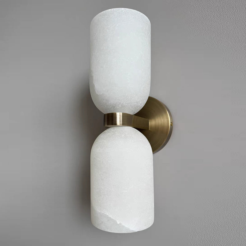 The Clérachic twin-cup alabaster sconce at an angle, polished brass band and round plate bright against a soft grey wall.