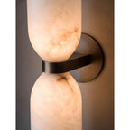 Close crop of the Clérachic sconce lit, amber light through the alabaster with dark veining tracing the stone above the brass band.