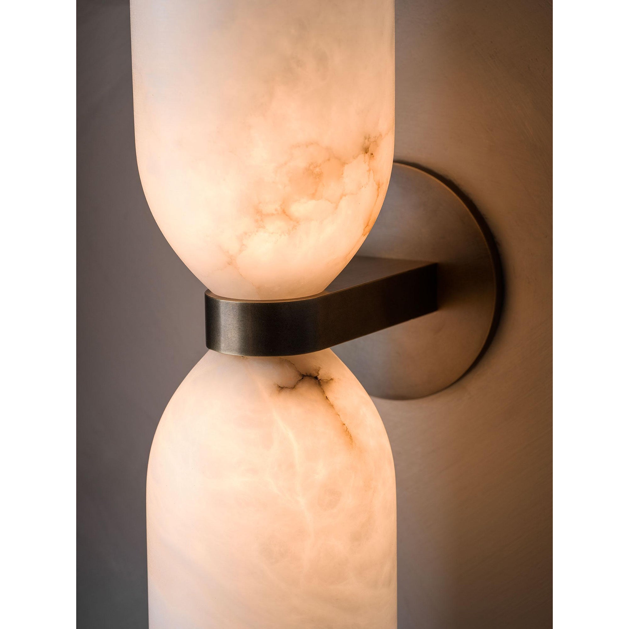 Close crop of the Clérachic sconce lit, amber light through the alabaster with dark veining tracing the stone above the brass band.