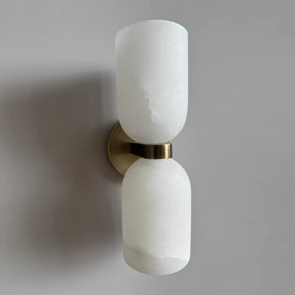 Clérachic alabaster wall sconce photographed from below, brass band catching the daylight while the stone reads cool white.