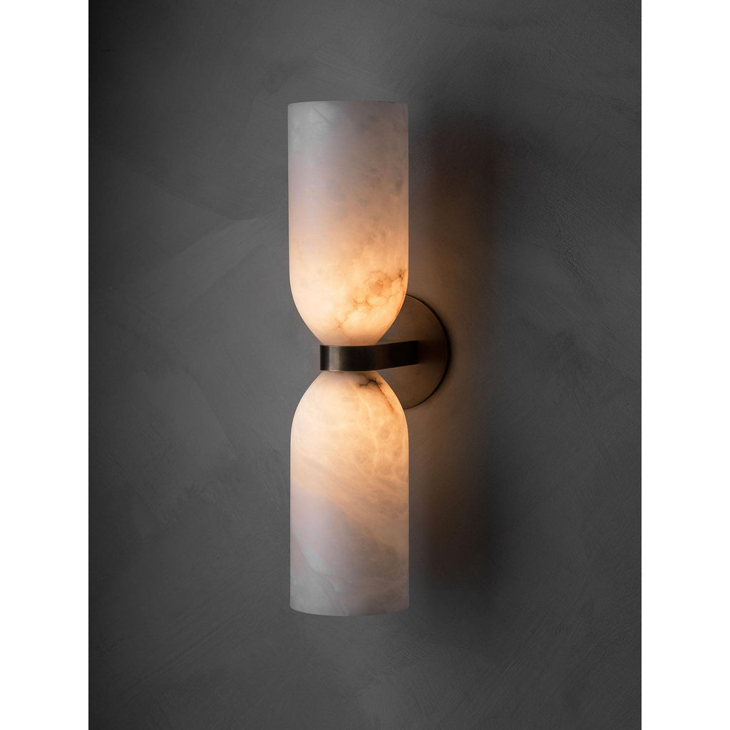 Clérachic twin alabaster cups glowing warm against a charcoal plaster wall, light leaving upward and downward from the sconce.