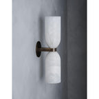 Angled view of the Clérachic wall sconce unlit, the aged brass arm and round plate reading warm against pale grey plaster.