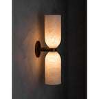 The Clérachic sconce lit in a darkened room, a soft halo of light behind the brass plate and no beam pointed at anything.