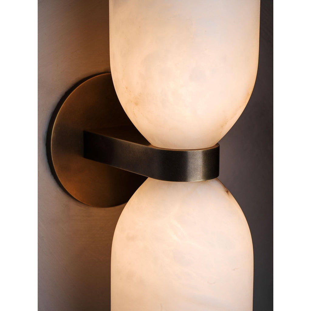 Close detail of the Clérachic sconce in use, the brass band dark against alabaster lit to honey on both sides of the waist.
