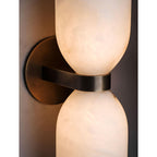 Close detail of the Clérachic sconce in use, the brass band dark against alabaster lit to honey on both sides of the waist.