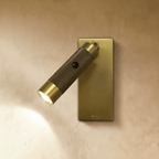 Clérachic wall reading light with a knurled dark bronze cylinder on a brushed brass rectangular plate, its beam lit on plaster.