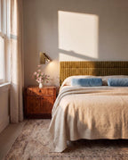 Clérachic small brass wall reading light over a burr-wood bedside cabinet, beside a bed with a striped velvet headboard.
