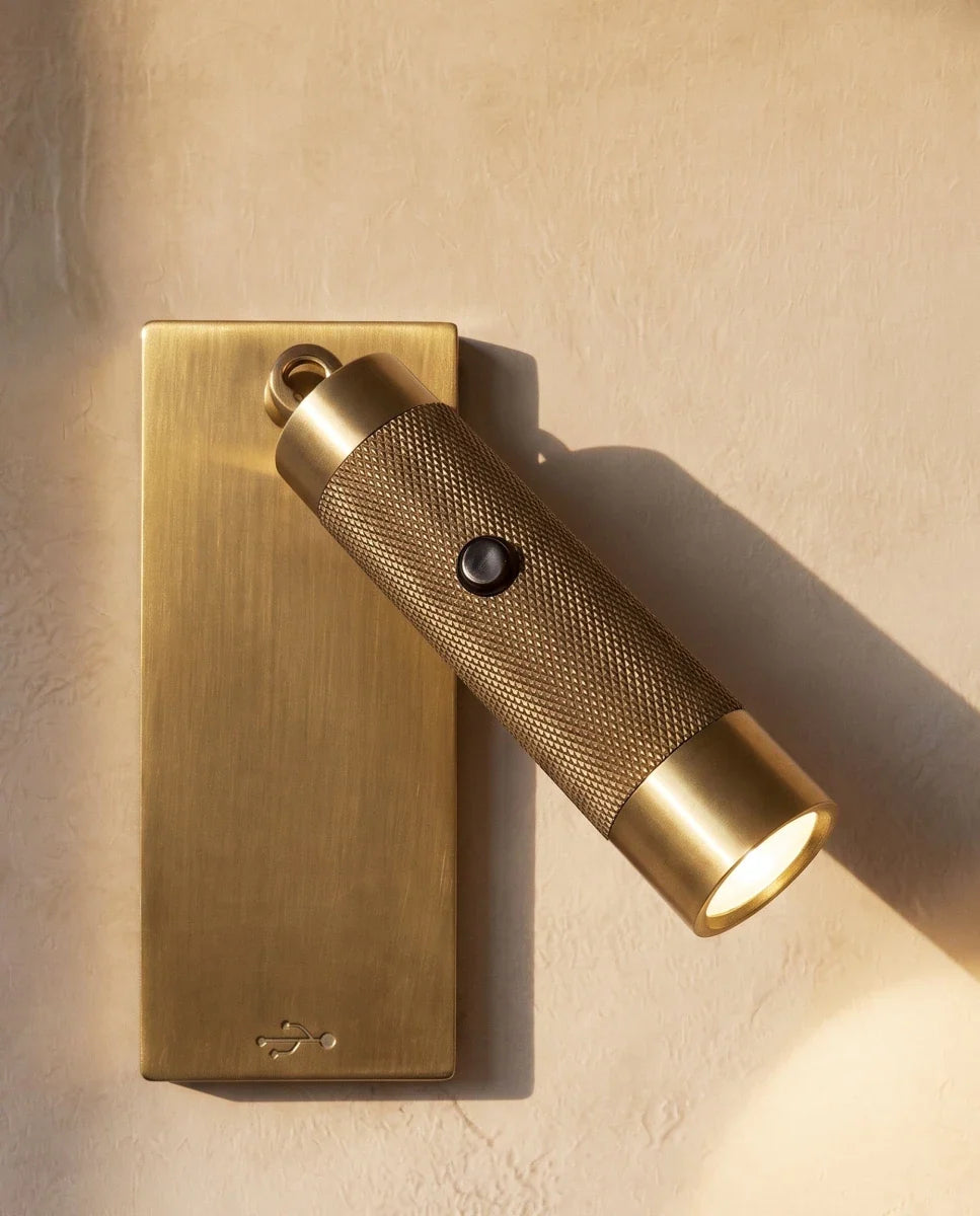 Close view of a Clérachic antique brass reading light, its knurled cylinder swung out with the beam on and a USB symbol on the plate.