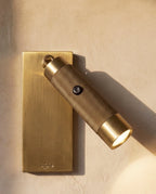 Close view of a Clérachic antique brass reading light, its knurled cylinder swung out with the beam on and a USB symbol on the plate.