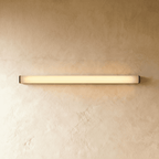 Clérachic slim linear wall light with a glowing frosted diffuser and black end caps, mounted horizontally on limewash plaster.