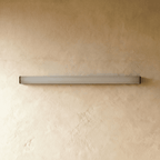 Clérachic slim linear wall light switched off, a frosted white diffuser tube with black end caps on warm plaster.