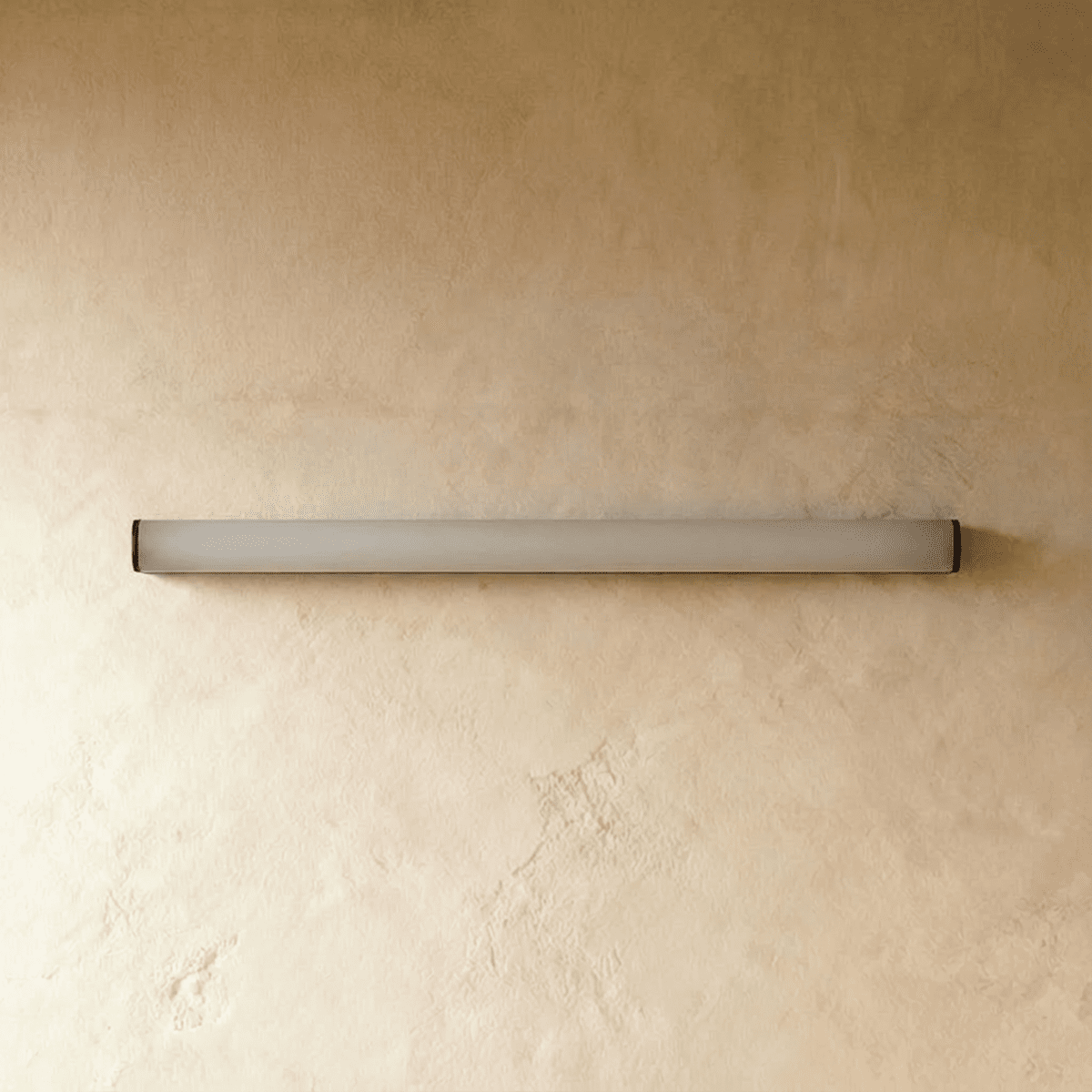 Clérachic slim linear wall light switched off, a frosted white diffuser tube with black end caps on warm plaster.