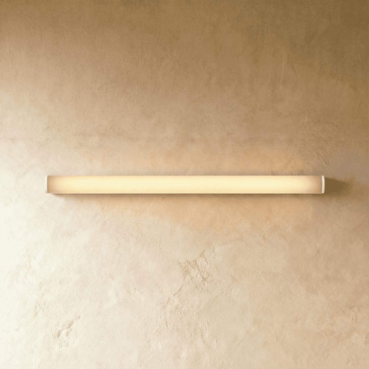 Clérachic slim linear wall light in white with a softly glowing diffuser, fixed horizontally on a warm limewash wall.