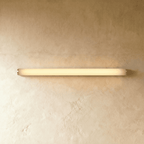Clérachic slim linear wall light with silver end caps and a warm glowing diffuser, mounted flat on textured plaster.