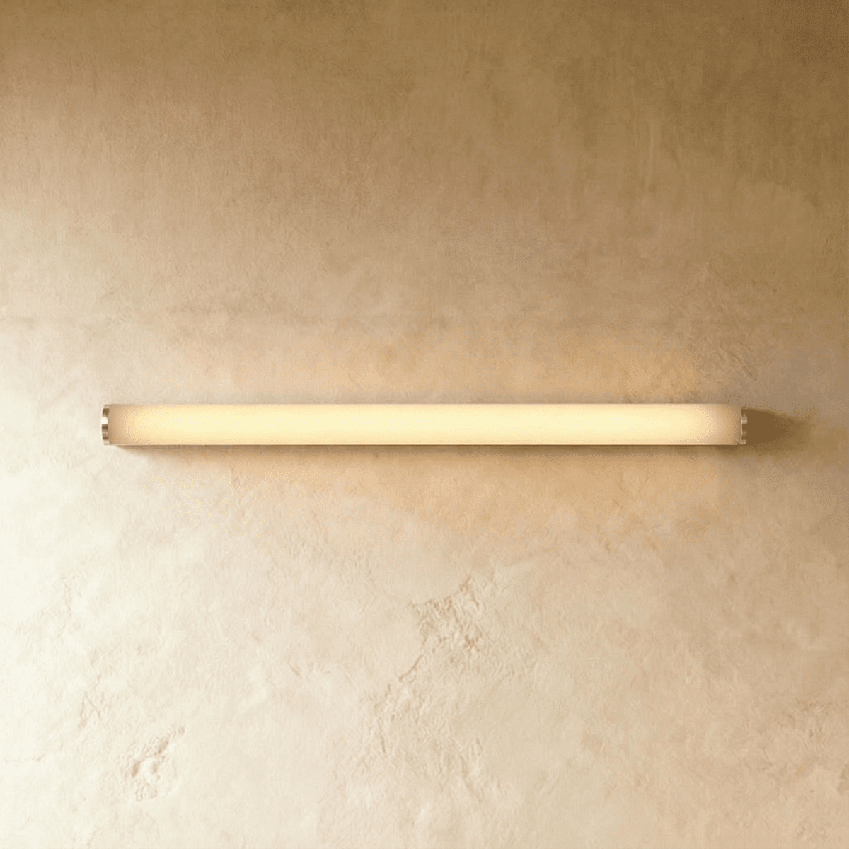 Clérachic slim linear wall light with silver end caps and a warm glowing diffuser, mounted flat on textured plaster.