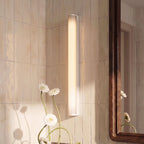 Clérachic white linear wall light mounted vertically on glossy cream tiles, with daisies and a walnut mirror frame beside it.