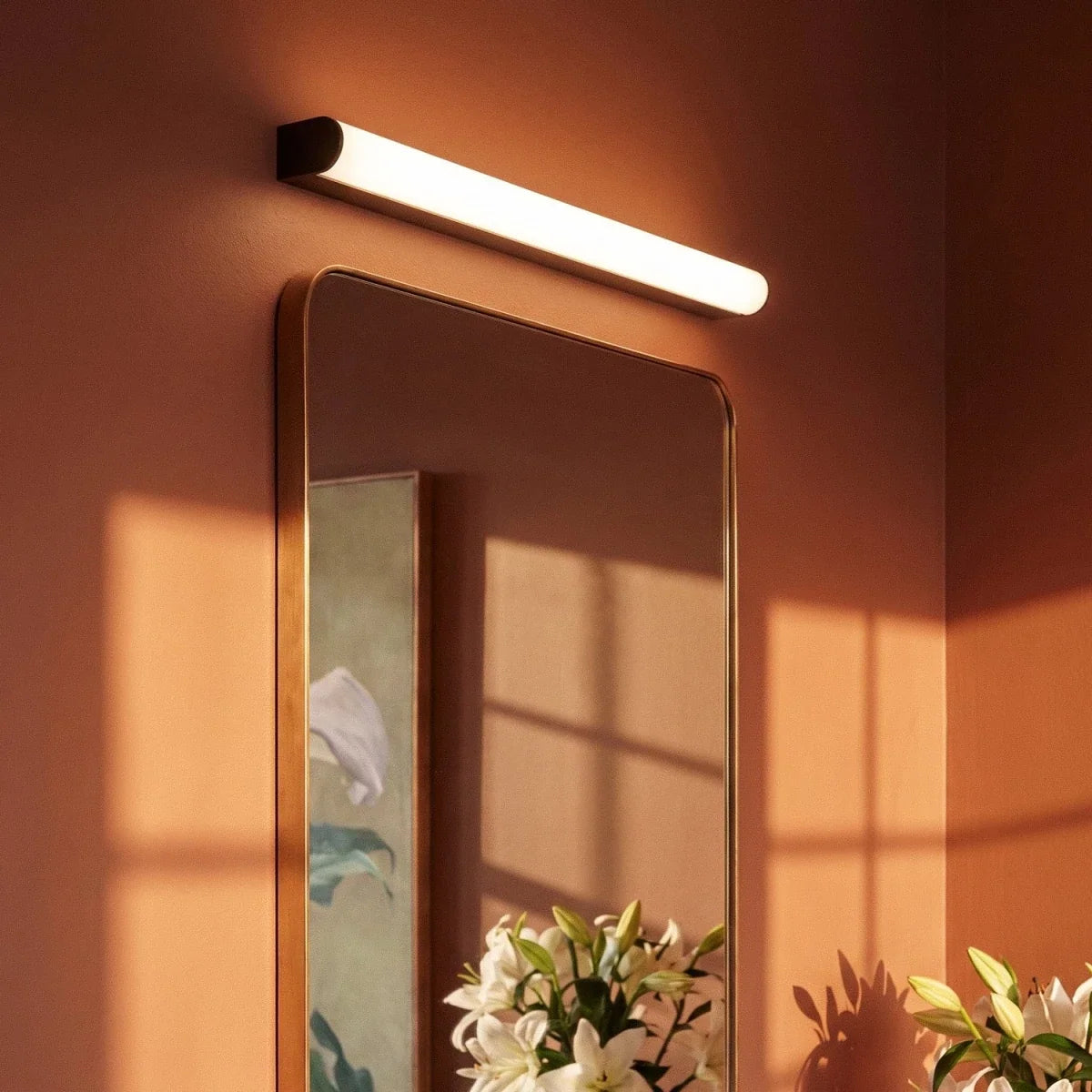 Clérachic linear wall light with a black end cap and bright frosted diffuser, fixed above a gold-framed mirror.
