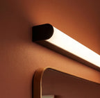 Close-up of the Clérachic linear wall light: a rounded black end cap and a smooth, glowing white diffuser on a terracotta wall.
