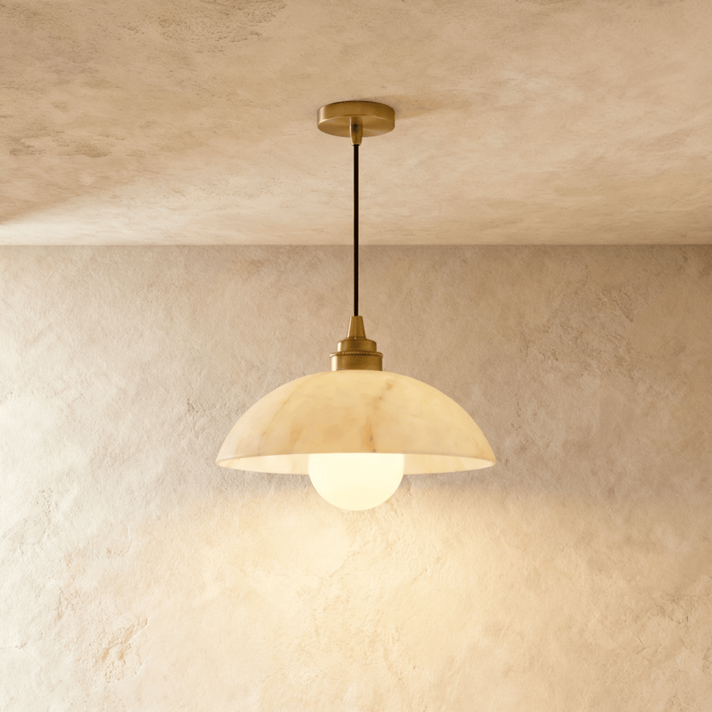 Clérachic pendant with a wide, softly veined alabaster dome and gold fitting, its opal globe bulb lit on plaster.