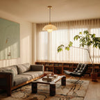Clérachic alabaster dome pendant hanging in a bright living room, with a sofa, low shelving, a tall plant and sheer curtains.