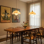 Two Clérachic alabaster dome pendants glowing over a wooden dining table, with woven chairs, framed art and sheer curtains.