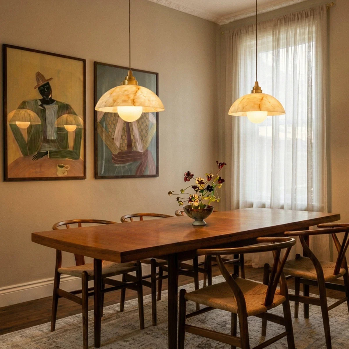 Two Clérachic alabaster dome pendants glowing over a wooden dining table, with woven chairs, framed art and sheer curtains.