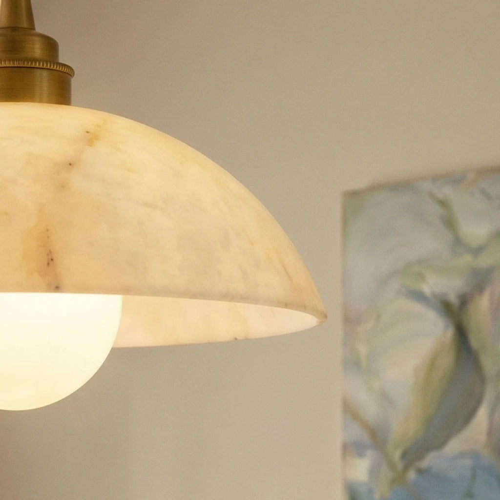Close view of a Clérachic alabaster dome edge, softly translucent, with the gold collar and a glowing globe bulb.