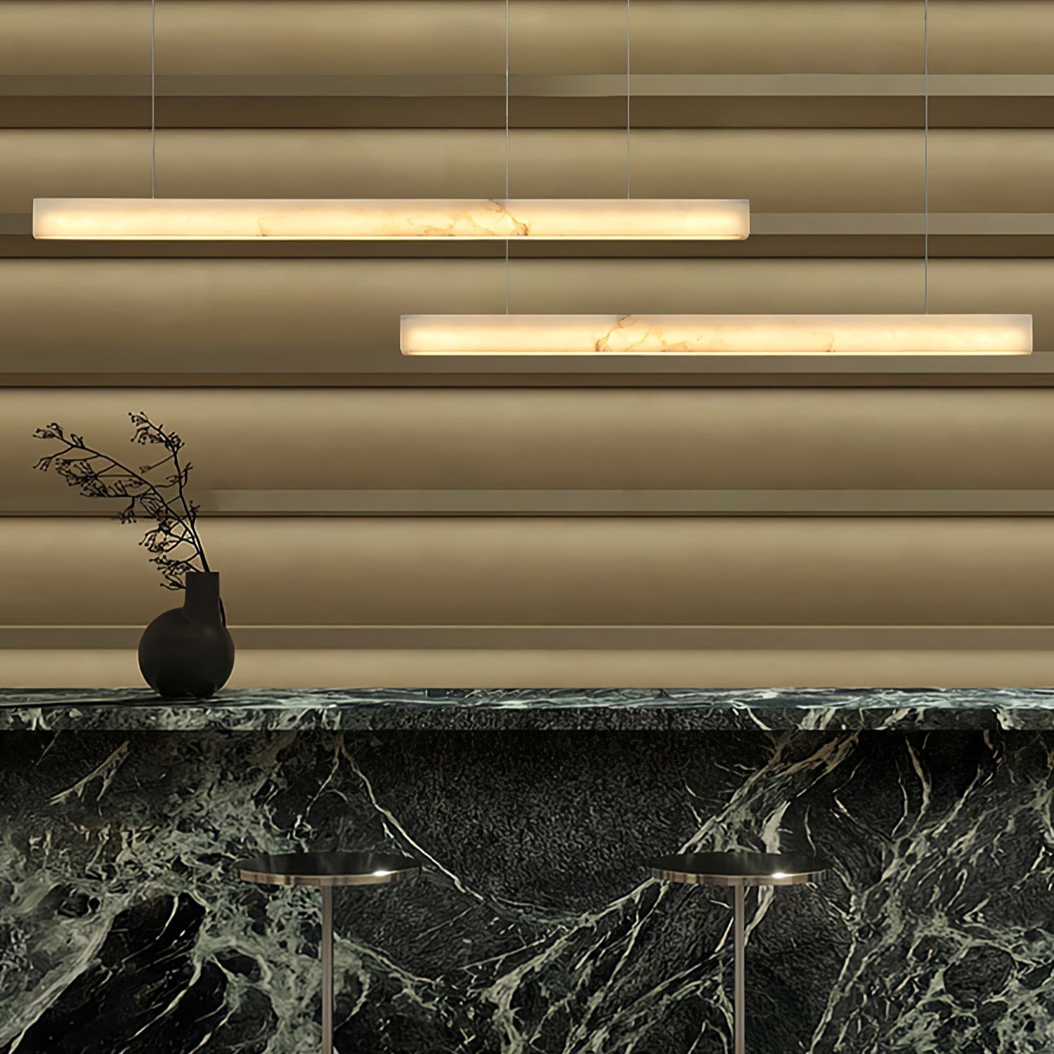 Two Clérachic Velmore pendants over a green marble counter with fluted brass panelling behind.