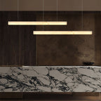 Clérachic Velmore pendants staggered above a veined marble counter and dark timber joinery.