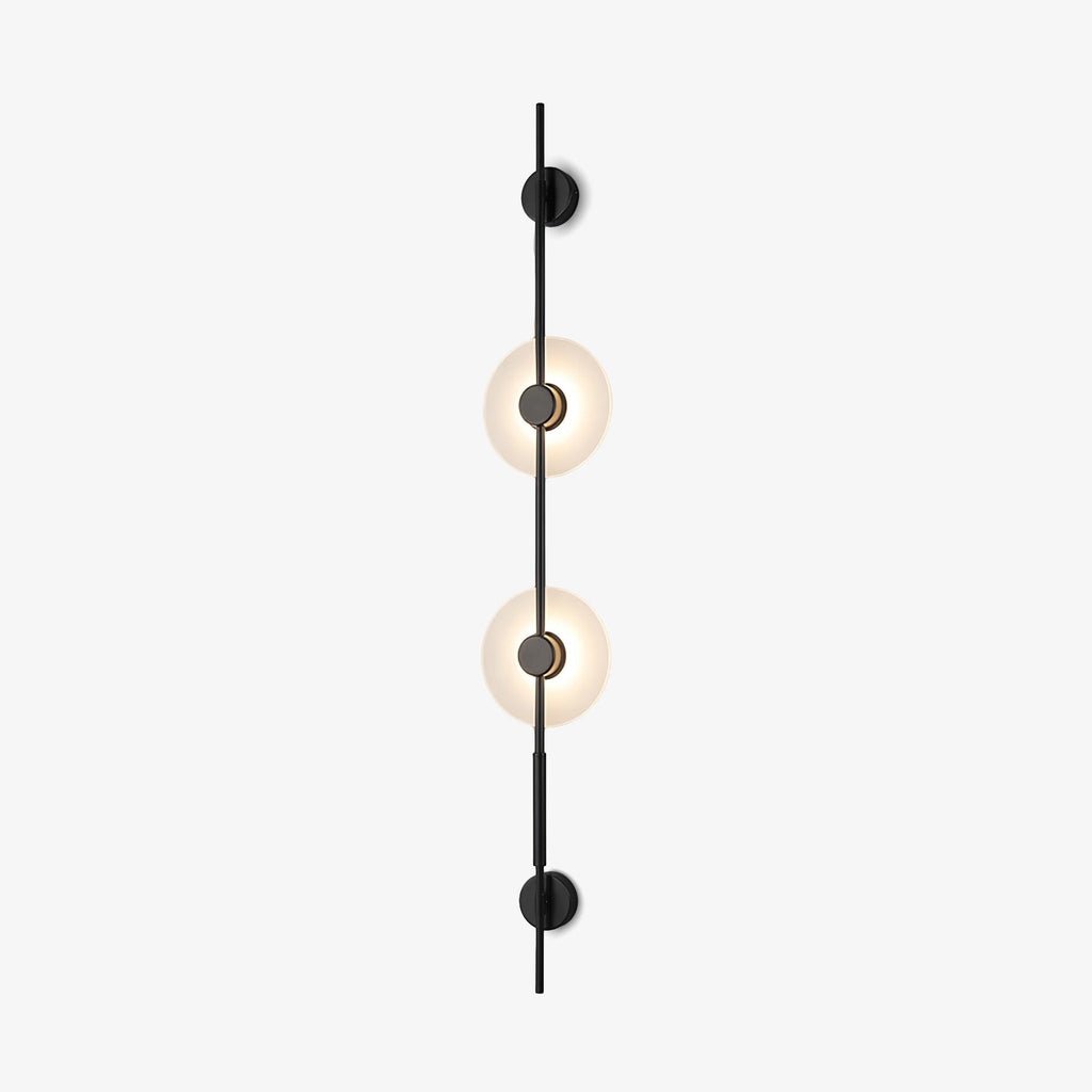 Front view of this Clérachic vertical wall sconce in black on a white backdrop, with two glowing alabaster discs on a slim upright rod.