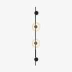 Front view of this Clérachic vertical wall sconce in black on a white backdrop, with two glowing alabaster discs on a slim upright rod.