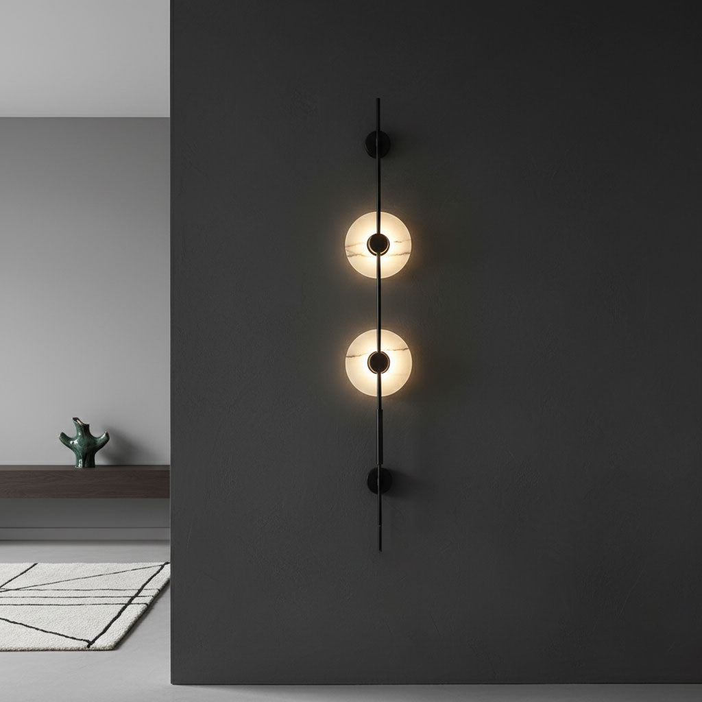 Two glowing alabaster discs on a black Clérachic sconce, set against a charcoal wall with a pale rug on the floor.