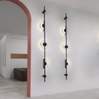 A pair of black three-disc Clérachic sconces on a white wall beside a terracotta-pink arch, with a lit room beyond.