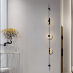 Tall black three-disc Clérachic sconce on a white panelled wall, with a small tree on a white stand at the left.